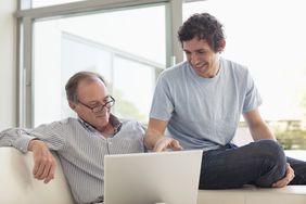 Adult son smiling and pointing to a laptop screen with his father