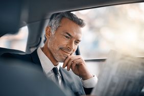 Cropped shot of a handsome mature businessman reading the paper while sitting in the backseat of a car during his morning commute