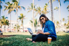 Millennial business owner working on laptop in park surrounded by palm trees