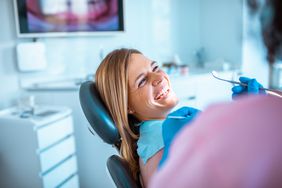 A woman sits in a dentist’s chair, smiling.