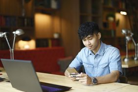 Young man holding credit card looks at smartphone in library