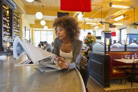 African American woman reading newspaper in cafe 