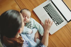 Mom working on a computer while holding sleeping baby