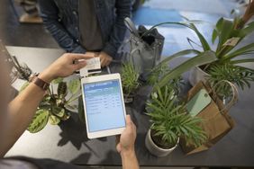 Overhead view male shop owner swiping digital tablet credit card payment in plant shop