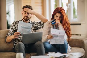A stressed couple sits on a sofa worrying over their credit card statement