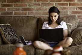 person on couch with computer on lap, sitting in front of brick wall