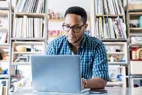 person with glasses in blue flannel shirt working on laptop