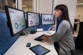 Financial analyst using multiple computer screens, tablet and smart phone at a workstation.