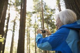 Senior woman photographing trees in woods