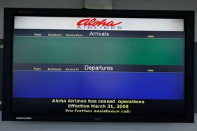 An airport info screen displays no arrivals nor departures for bankrupt airline Aloha Airlines.