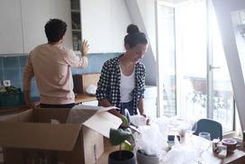 A young couple open moving boxes containing kitchen tools and supplies in a clean, well-lighted place.