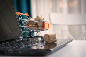 Miniature shopping cart full of packages on keyboard of a laptop