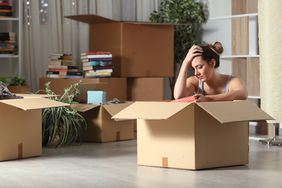 A woman sits on the floor amid moving boxes looking stressed.