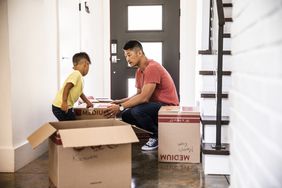  A man and a young boy move boxes into an empty home. 