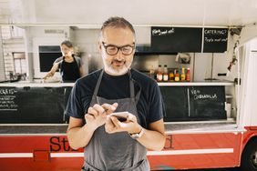 Chef in apron uses smartphone in front of food truck