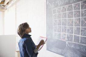 Woman with folders in her hands looking at a calendar written on a blackboard