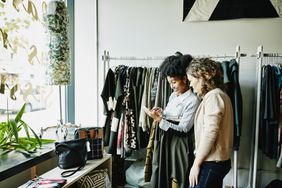 Two women look at a phone in a boutique.
