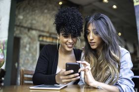 Two women, sitting at a cafe, looking into a smart phone