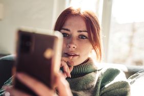 A woman looks with curiosity at a smartphone screen.