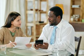 Adult Black man and young white woman sitting at table and talking with papers
