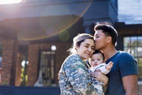 Soldier holding baby is kissed by her husband