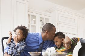 Father kissing sons at breakfast table.