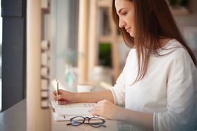 Young woman writing in an appointment book, glasses on desk