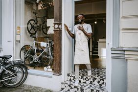 Bicycle shop employee in apron smiles at store entrance