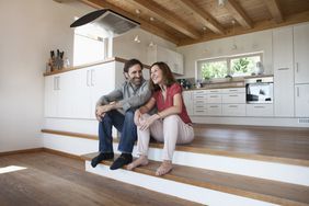 New homeowners seated on a step in their kitchen