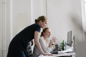 Two women look at a computer screen.