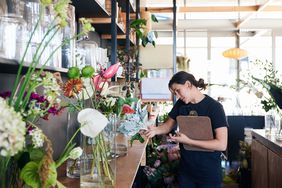 Female florist stands in shop while talking on phone