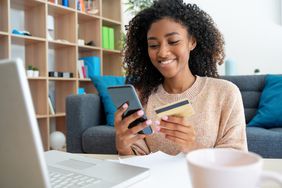 Cheerful young black woman using credit card at home