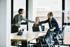 Two business people shake hands over a conference room table