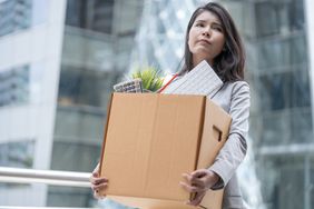 Unemployed businesswoman carrying a cardboard box out of an office