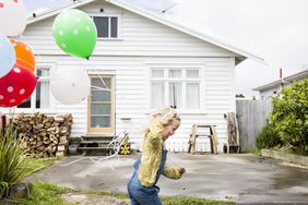A child holds balloons while running in front of a house