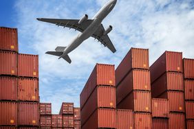 A plane flying over a shipping yard with stacks of shipping containers