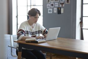 Young person in sweater looks at laptop on table