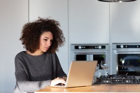 Young adult woman uses laptop on kitchen island