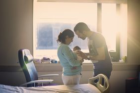 Two people hold a baby in a hospital room.