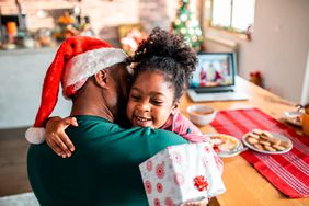 Child holding a gift hugging her father who's wearing a Santa hat
