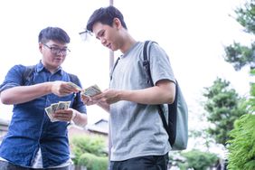 Young man handing dollars to and lending money to friend