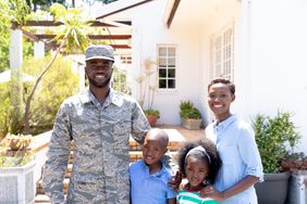 A soldier and his family stand in front of a house