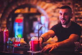 Close-up of young bartender serving cocktail in nightlife bar