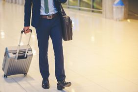 Man's legs wearing blue dress pants pulling suitcase through airport