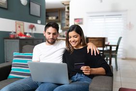 Couple shopping on laptop sitting on sofa in living room at home