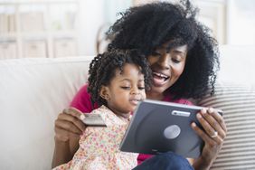 Mother holding credit card and daughter look at digital tablet