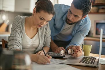 Worried couple working at kitchen table paying bills when money is tight.