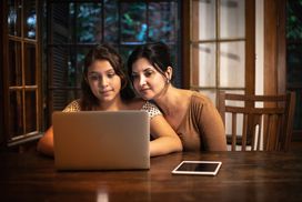 mom and daughter sitting at a wooden table looking at computer