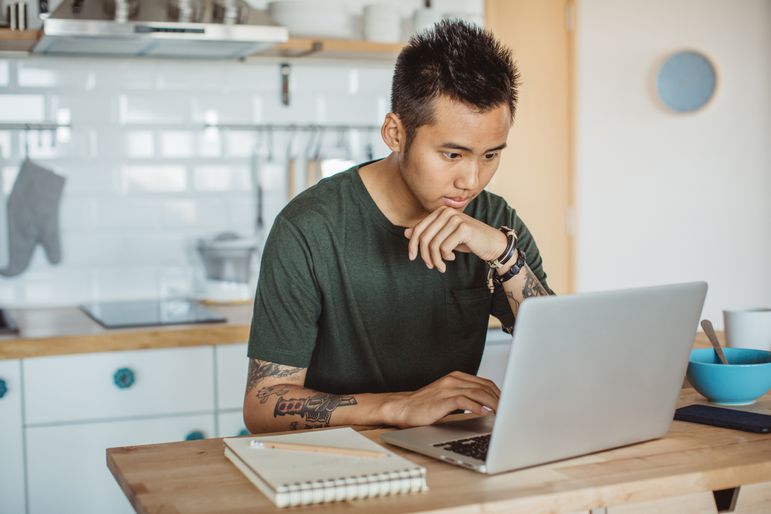 Young person focused on laptop at kitchen counter