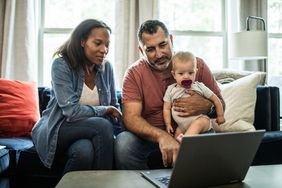 Husband and wife holding baby and looking at laptop